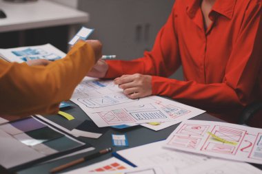 Uxui tasarımcılarından oluşan bir ekip bilgisayar ekranını işaret ederek ofiste yeni mobil uygulama tasarımını tartışıyor.