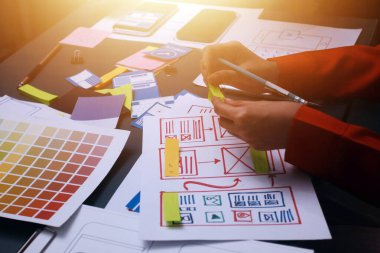 Uxui tasarımcılarından oluşan bir ekip bilgisayar ekranını işaret ederek ofiste yeni mobil uygulama tasarımını tartışıyor.