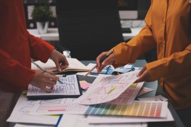 Uxui tasarımcılarından oluşan bir ekip bilgisayar ekranını işaret ederek ofiste yeni mobil uygulama tasarımını tartışıyor.