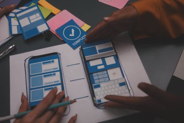 Uxui tasarımcılarından oluşan bir ekip bilgisayar ekranını işaret ederek ofiste yeni mobil uygulama tasarımını tartışıyor.