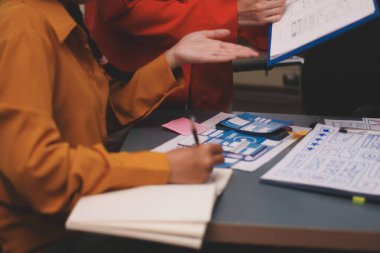 Uxui tasarımcılarından oluşan bir ekip bilgisayar ekranını işaret ederek ofiste yeni mobil uygulama tasarımını tartışıyor.