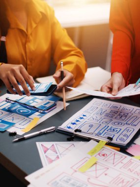 Uxui tasarımcılarından oluşan bir ekip bilgisayar ekranını işaret ederek ofiste yeni mobil uygulama tasarımını tartışıyor.