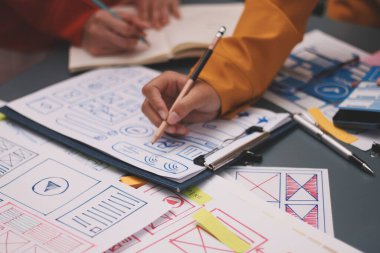 Uxui tasarımcılarından oluşan bir ekip bilgisayar ekranını işaret ederek ofiste yeni mobil uygulama tasarımını tartışıyor.