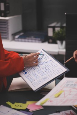 Uxui tasarımcılarından oluşan bir ekip bilgisayar ekranını işaret ederek ofiste yeni mobil uygulama tasarımını tartışıyor.