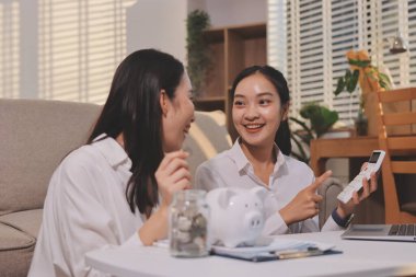 Mutlu Asyalı genç çift hesap yapıyor, kumbaraya para koyuyor yeni ev almak için para biriktiriyorlar. İş finansmanı, birlikte finansal planlama için banka mevduatı