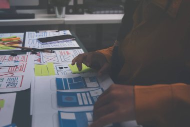 Uxui tasarımcılarından oluşan bir ekip bilgisayar ekranını işaret ederek ofiste yeni mobil uygulama tasarımını tartışıyor.