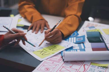 Uxui tasarımcılarından oluşan bir ekip bilgisayar ekranını işaret ederek ofiste yeni mobil uygulama tasarımını tartışıyor.