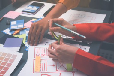 Uxui tasarımcılarından oluşan bir ekip bilgisayar ekranını işaret ederek ofiste yeni mobil uygulama tasarımını tartışıyor.