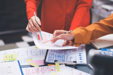 Uxui tasarımcılarından oluşan bir ekip bilgisayar ekranını işaret ederek ofiste yeni mobil uygulama tasarımını tartışıyor.