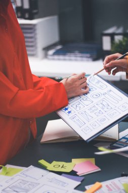 Uxui tasarımcılarından oluşan bir ekip bilgisayar ekranını işaret ederek ofiste yeni mobil uygulama tasarımını tartışıyor.