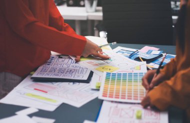 Uxui tasarımcılarından oluşan bir ekip bilgisayar ekranını işaret ederek ofiste yeni mobil uygulama tasarımını tartışıyor.