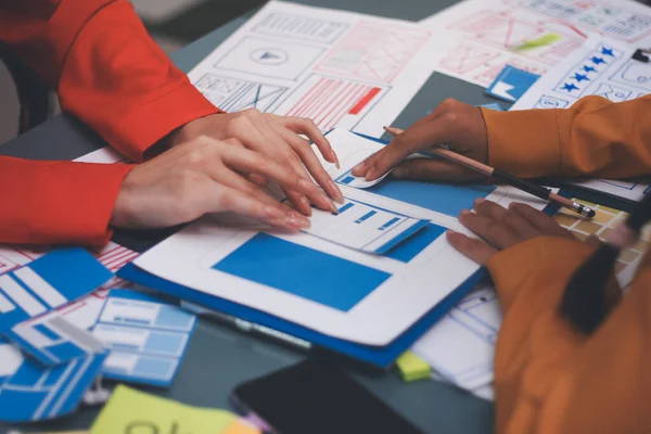 Uxui tasarımcılarından oluşan bir ekip bilgisayar ekranını işaret ederek ofiste yeni mobil uygulama tasarımını tartışıyor.