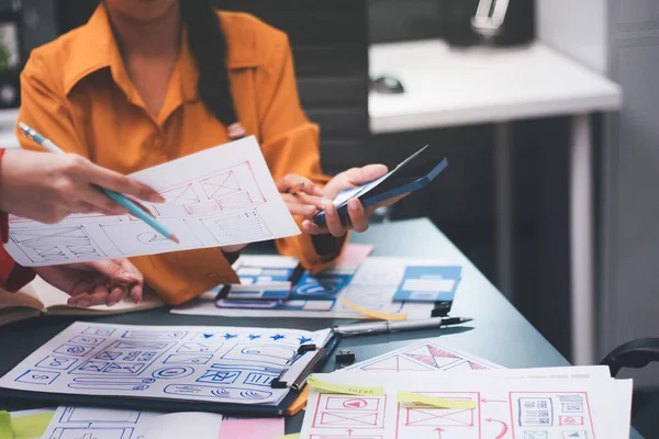 Uxui tasarımcılarından oluşan bir ekip bilgisayar ekranını işaret ederek ofiste yeni mobil uygulama tasarımını tartışıyor.