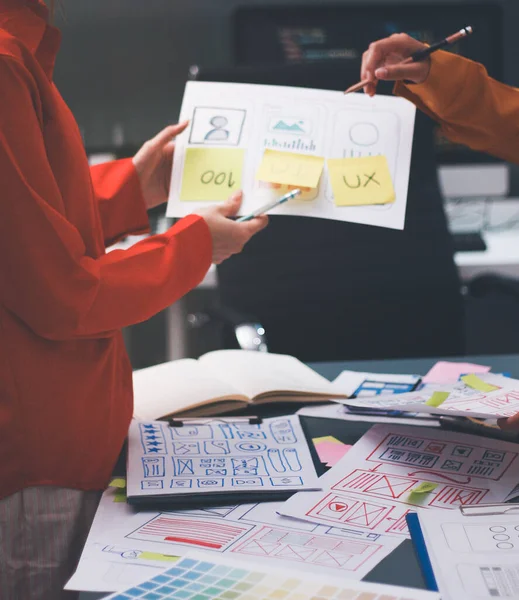 Uxui tasarımcılarından oluşan bir ekip bilgisayar ekranını işaret ederek ofiste yeni mobil uygulama tasarımını tartışıyor.