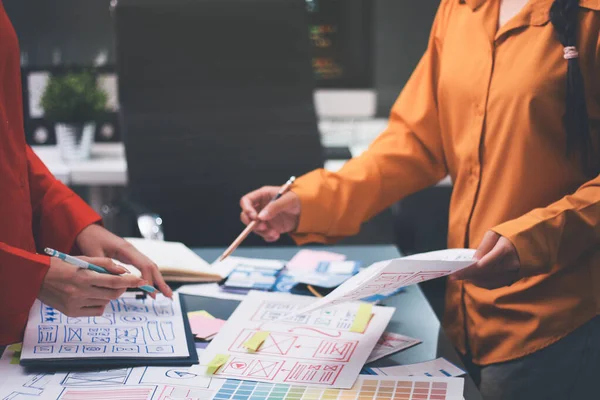 Uxui tasarımcılarından oluşan bir ekip bilgisayar ekranını işaret ederek ofiste yeni mobil uygulama tasarımını tartışıyor.