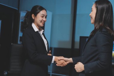 İki Asyalı iş kadını şirket stratejisini tartışıyorlar. Gece ofiste dizüstü bilgisayar ve grafikler kullanıyorlar.