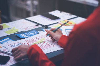 Uxui tasarımcılarından oluşan bir ekip bilgisayar ekranını işaret ederek ofiste yeni mobil uygulama tasarımını tartışıyor.