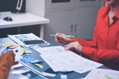 Uxui tasarımcılarından oluşan bir ekip bilgisayar ekranını işaret ederek ofiste yeni mobil uygulama tasarımını tartışıyor.