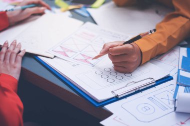 Uxui tasarımcılarından oluşan bir ekip bilgisayar ekranını işaret ederek ofiste yeni mobil uygulama tasarımını tartışıyor.