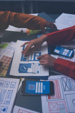 Uxui tasarımcılarından oluşan bir ekip bilgisayar ekranını işaret ederek ofiste yeni mobil uygulama tasarımını tartışıyor.