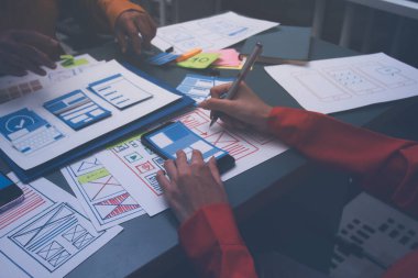 Uxui tasarımcılarından oluşan bir ekip bilgisayar ekranını işaret ederek ofiste yeni mobil uygulama tasarımını tartışıyor.