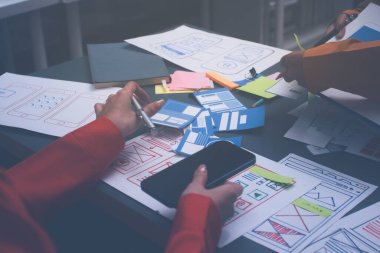 Uxui tasarımcılarından oluşan bir ekip bilgisayar ekranını işaret ederek ofiste yeni mobil uygulama tasarımını tartışıyor.