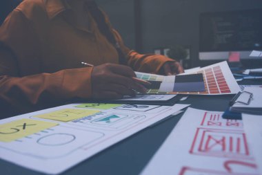 Uxui tasarımcılarından oluşan bir ekip bilgisayar ekranını işaret ederek ofiste yeni mobil uygulama tasarımını tartışıyor.