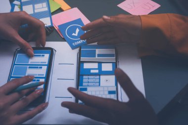 Uxui tasarımcılarından oluşan bir ekip bilgisayar ekranını işaret ederek ofiste yeni mobil uygulama tasarımını tartışıyor.