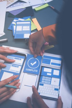 Uxui tasarımcılarından oluşan bir ekip bilgisayar ekranını işaret ederek ofiste yeni mobil uygulama tasarımını tartışıyor.