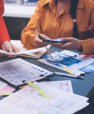 Uxui tasarımcılarından oluşan bir ekip bilgisayar ekranını işaret ederek ofiste yeni mobil uygulama tasarımını tartışıyor.