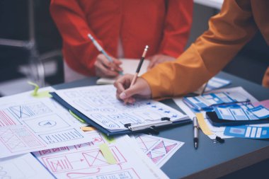 Uxui tasarımcılarından oluşan bir ekip bilgisayar ekranını işaret ederek ofiste yeni mobil uygulama tasarımını tartışıyor.