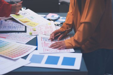 Uxui tasarımcılarından oluşan bir ekip bilgisayar ekranını işaret ederek ofiste yeni mobil uygulama tasarımını tartışıyor.