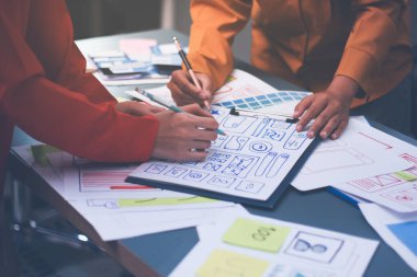 Uxui tasarımcılarından oluşan bir ekip bilgisayar ekranını işaret ederek ofiste yeni mobil uygulama tasarımını tartışıyor.