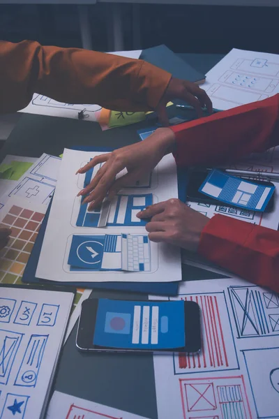 Uxui tasarımcılarından oluşan bir ekip bilgisayar ekranını işaret ederek ofiste yeni mobil uygulama tasarımını tartışıyor.