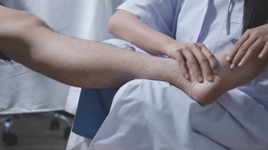 Doktor fizyoterapist yaralı dizini tedavi ediyor, sapını hastanın dizine dayayıp ağrısını kontrol ediyor..
