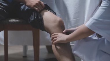 Doktor fizyoterapist yaralı dizini tedavi ediyor, sapını hastanın dizine dayayıp ağrısını kontrol ediyor..