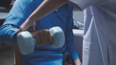 Evde fizyoterapistle egzersiz yapan mutlu yaşlı kadın. Emekli bir kadın rehabilitasyon seansı sırasında kişisel antrenörünün yardımıyla evde kollarını esnetiyor..