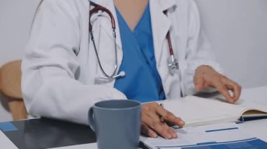 close - up of a female doctor writing a prescription on clipboard in hospital office.