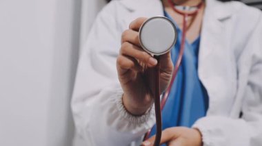 female doctor in white uniform holds stethoscope and shows thumb up, showing heart