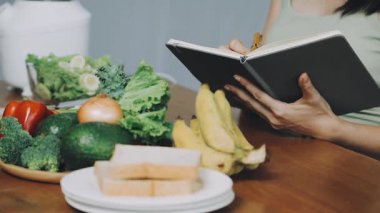 Genç bir kadın kitap okuyor ve kahvaltı yapıyor.