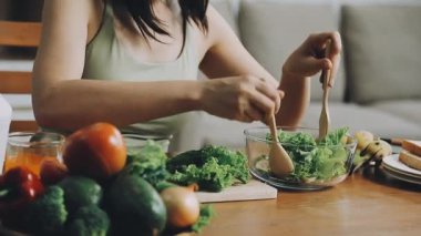 Modern mutfaktaki ahşap masanın üzerinde taze sebzelerle salata yapan kadın eli. Ev dekorasyonu. vejetaryen yemeği ve sağlıklı yaşam tarzı