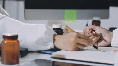 Beyaz gömlekli, siyah ceketli, kalemli, tahta masaya kalem yazan genç bir adam.