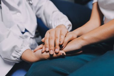 Doktor umut veriyor. Genç kadın hekimin avuçlarında elini tutan yaşlı bayanın gülümsemesini yakından çek. Beyaz önlüklü kadın bakıcı yaşlı insanı cesaretlendiriyor.