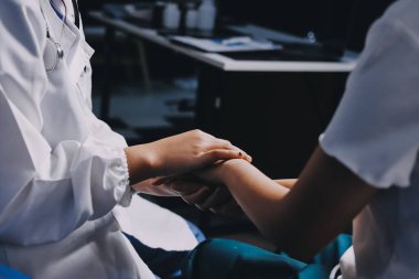 Doktor umut veriyor. Genç kadın hekimin avuçlarında elini tutan yaşlı bayanın gülümsemesini yakından çek. Beyaz önlüklü kadın bakıcı yaşlı insanı cesaretlendiriyor.