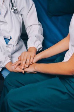 Doktor umut veriyor. Genç kadın hekimin avuçlarında elini tutan yaşlı bayanın gülümsemesini yakından çek. Beyaz önlüklü kadın bakıcı yaşlı insanı cesaretlendiriyor.