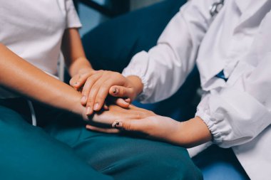 Doktor umut veriyor. Genç kadın hekimin avuçlarında elini tutan yaşlı bayanın gülümsemesini yakından çek. Beyaz önlüklü kadın bakıcı yaşlı insanı cesaretlendiriyor.