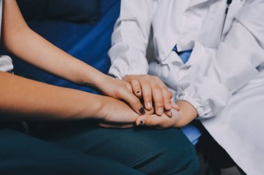 Doktor umut veriyor. Genç kadın hekimin avuçlarında elini tutan yaşlı bayanın gülümsemesini yakından çek. Beyaz önlüklü kadın bakıcı yaşlı insanı cesaretlendiriyor.