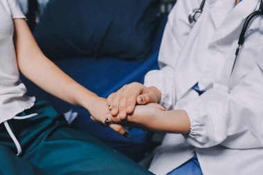 Doktor umut veriyor. Genç kadın hekimin avuçlarında elini tutan yaşlı bayanın gülümsemesini yakından çek. Beyaz önlüklü kadın bakıcı yaşlı insanı cesaretlendiriyor.