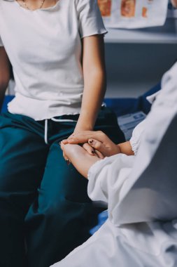 Doktor umut veriyor. Genç kadın hekimin avuçlarında elini tutan yaşlı bayanın gülümsemesini yakından çek. Beyaz önlüklü kadın bakıcı yaşlı insanı cesaretlendiriyor.