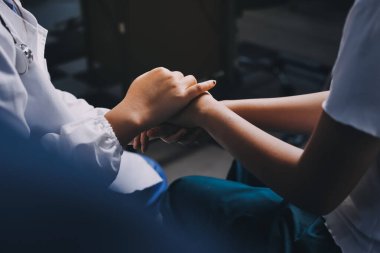 Doktor umut veriyor. Genç kadın hekimin avuçlarında elini tutan yaşlı bayanın gülümsemesini yakından çek. Beyaz önlüklü kadın bakıcı yaşlı insanı cesaretlendiriyor.